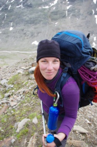 Susi mit roten Haaren und Bergrucksack und Kletterseil in den Alpen an einem Geröllhang